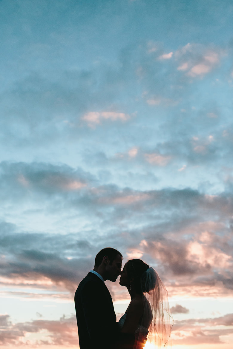 couple kiss on wedding day silhouette against dramatic sky